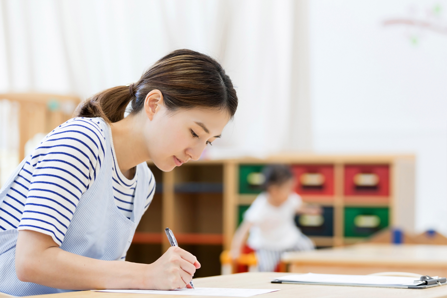 保育室で記録を書く保育士と遊ぶ子ども